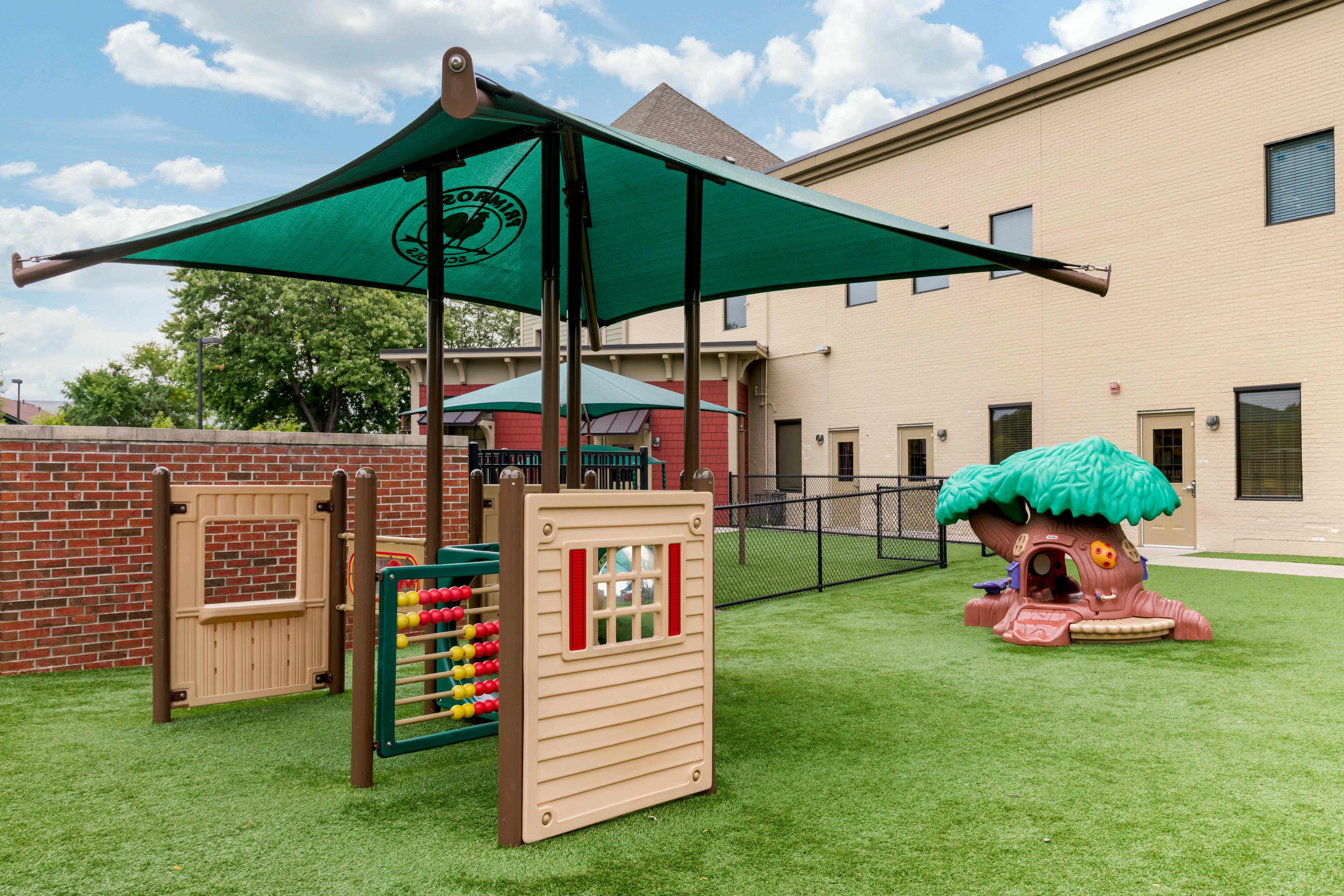 Outdoor playground with artificial grass, shaded play structure, abacus, and treehouse