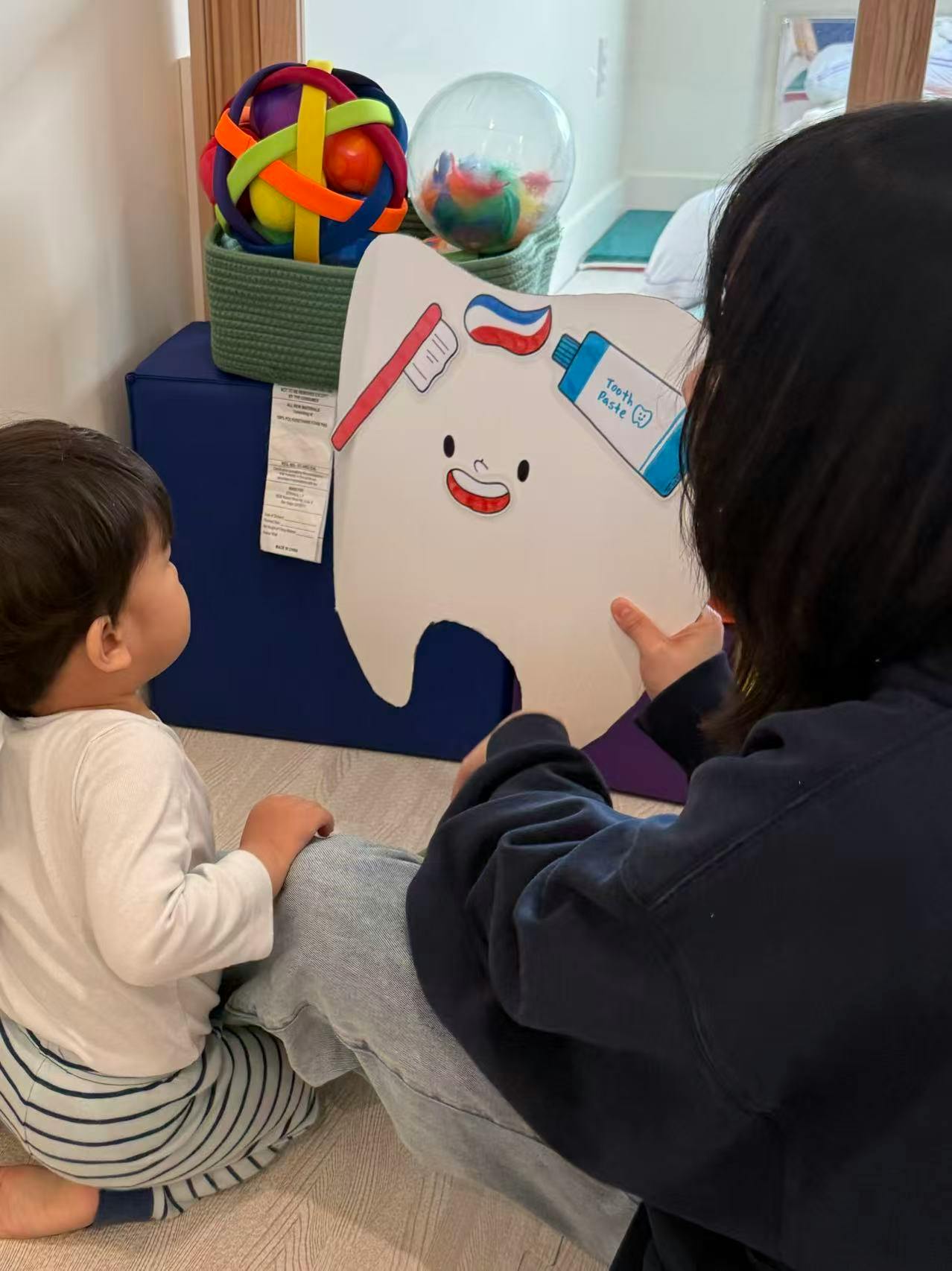Person showing a child a cartoon tooth with a toothbrush and toothpaste