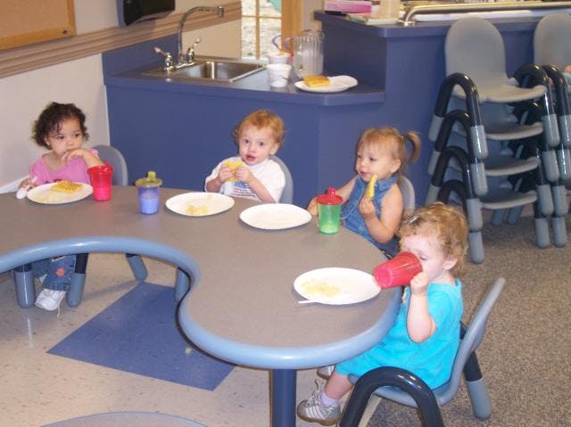 Four children eating at a table in a classroom