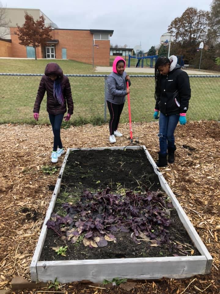 Three children working in a raised garden bed