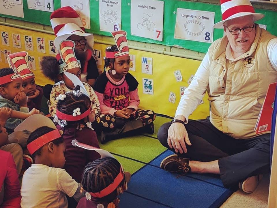 Person in striped hat reading to children in classroom