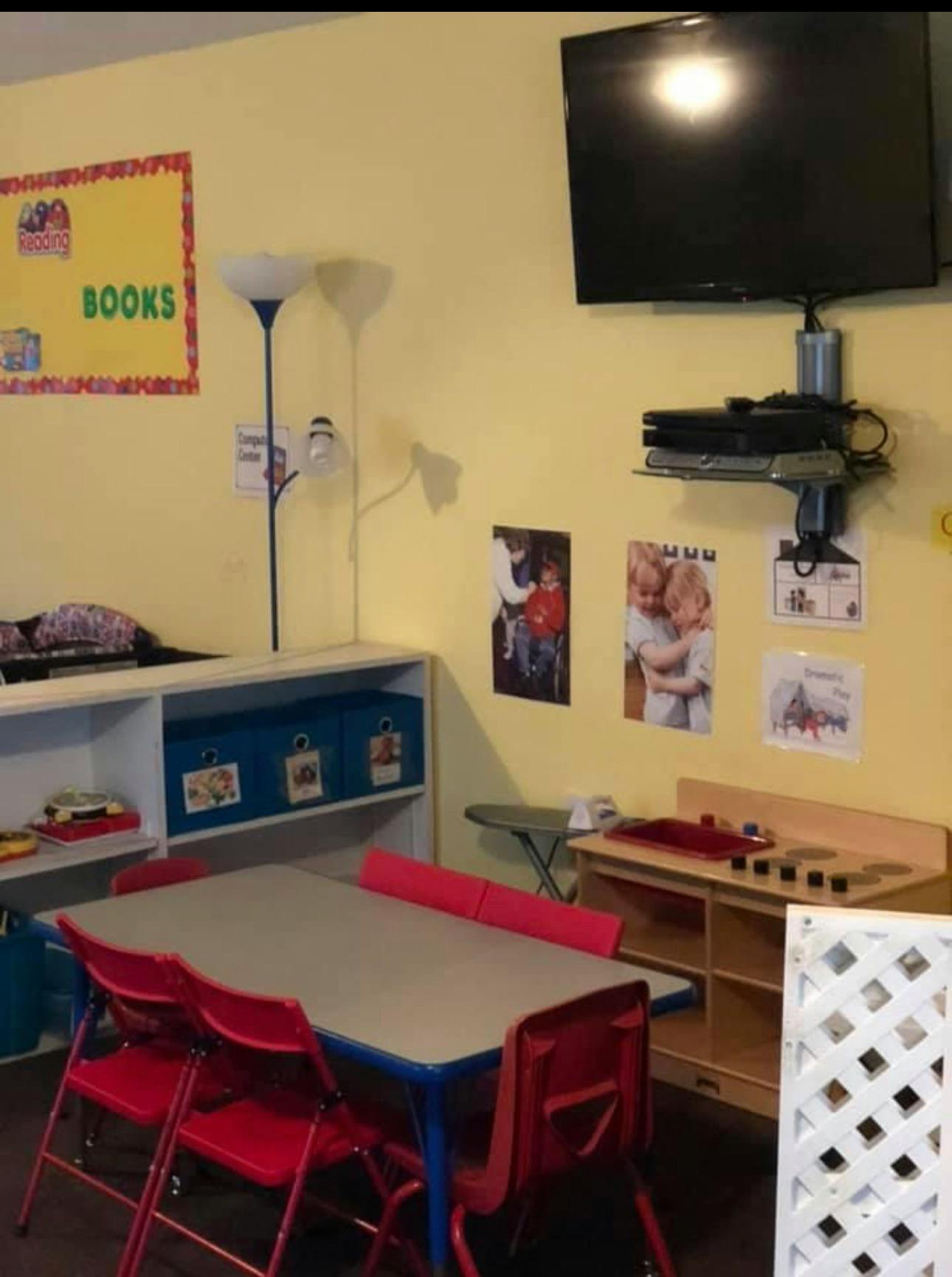 Classroom with a table and red chairs, shelves, and a wall-mounted TV