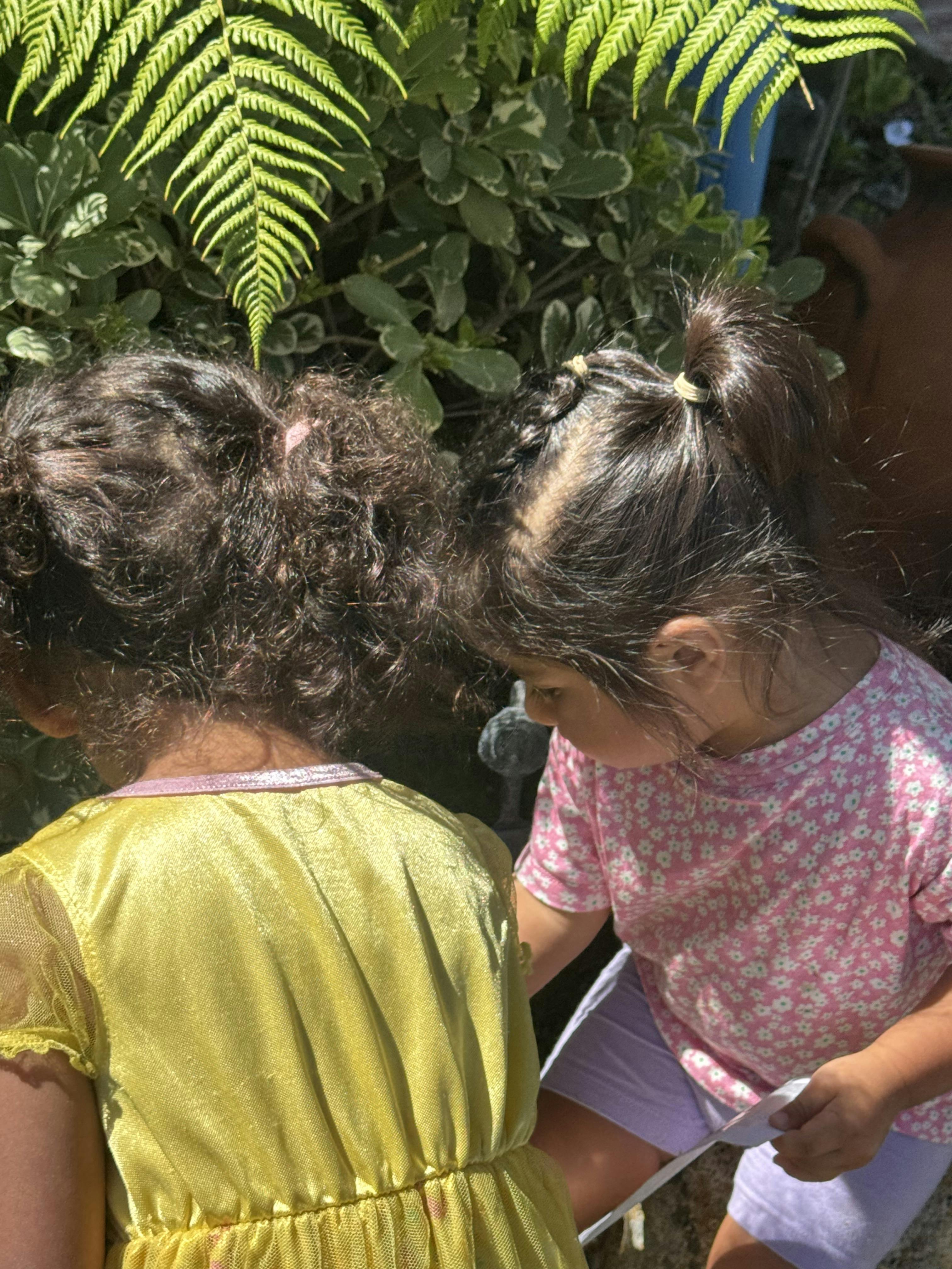 Two children looking down at something, one in a yellow dress, one in a pink shirt