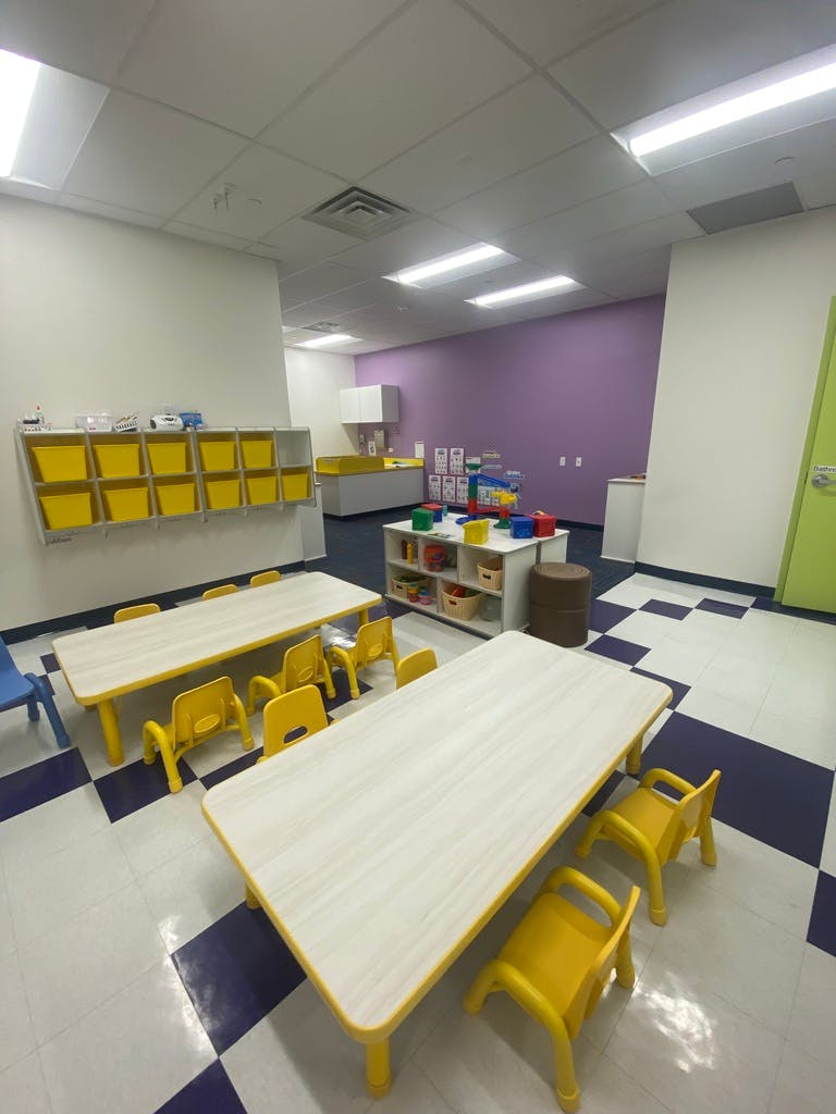 Classroom with small tables and chairs, storage shelves with yellow bins