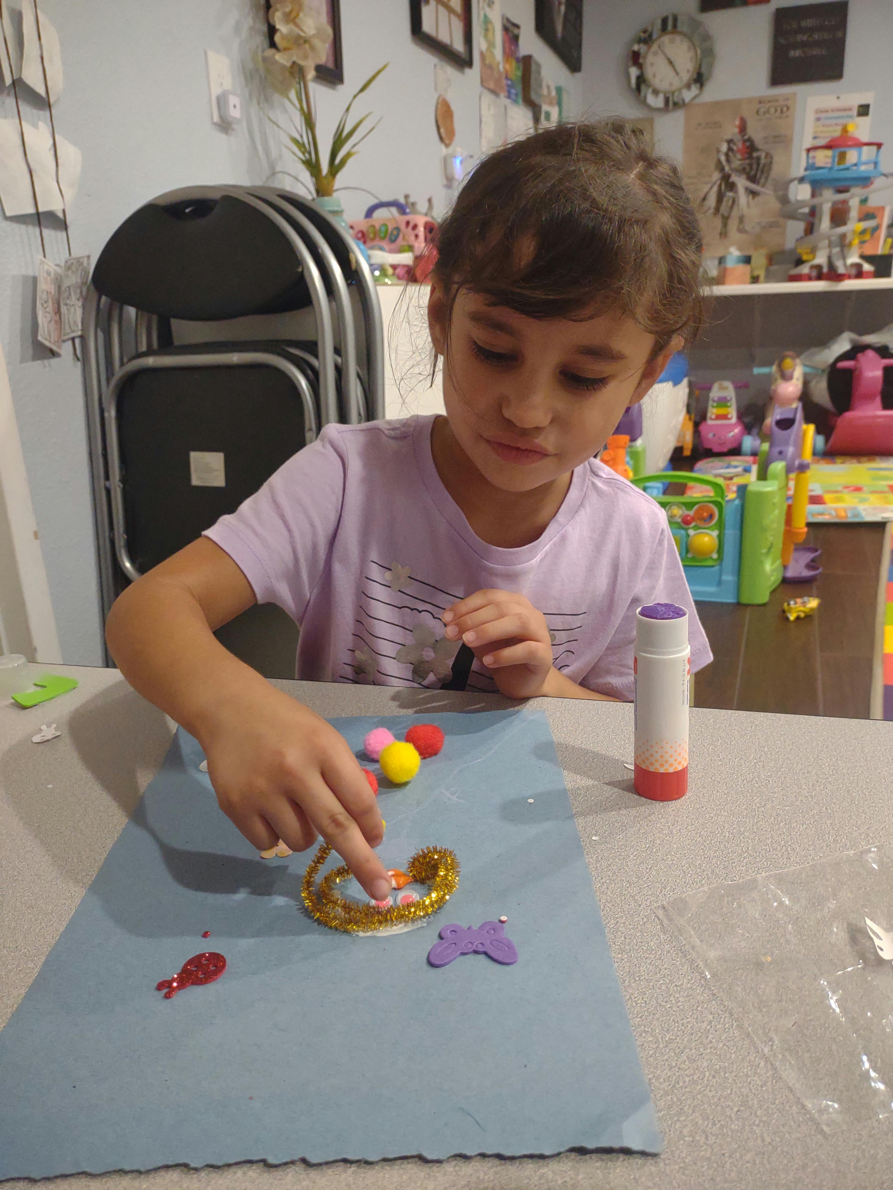 Child decorating a craft with glitter and pom-poms