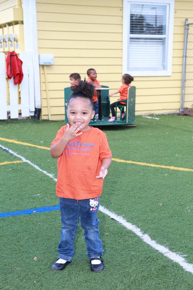 Child standing on artificial turf with other children in background
