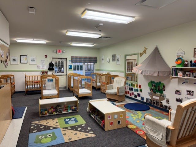 A daycare room with multiple cribs, a play tent, and activity rugs