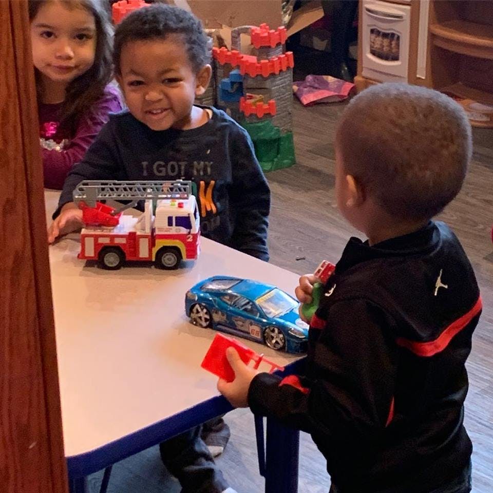 Three children playing with toy cars at a table