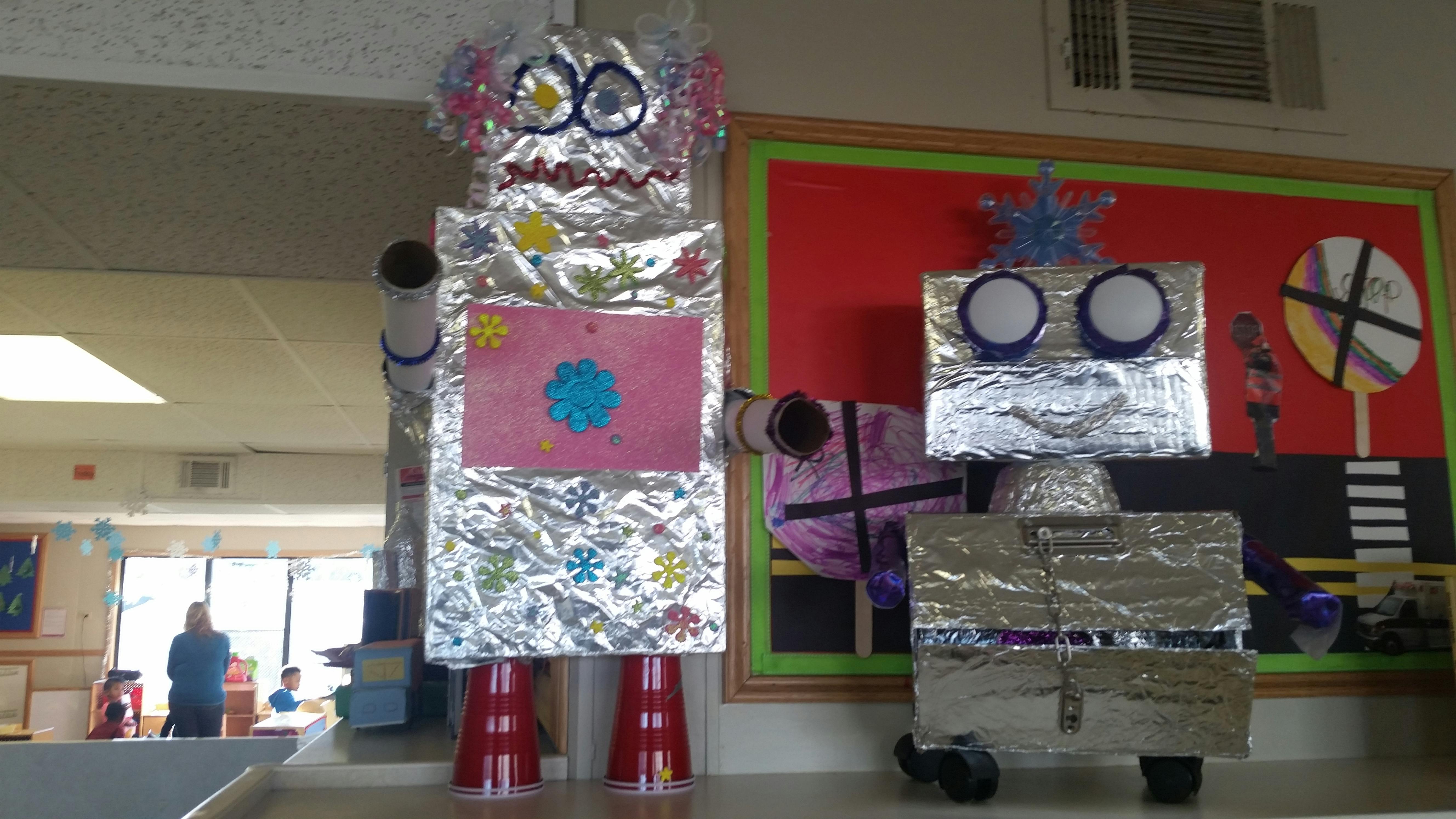 Two robots made from cardboard boxes and aluminum foil decorated with craft items