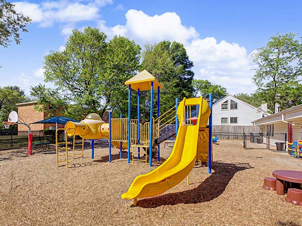 Playground with yellow slides, climbing structure, and basketball hoop