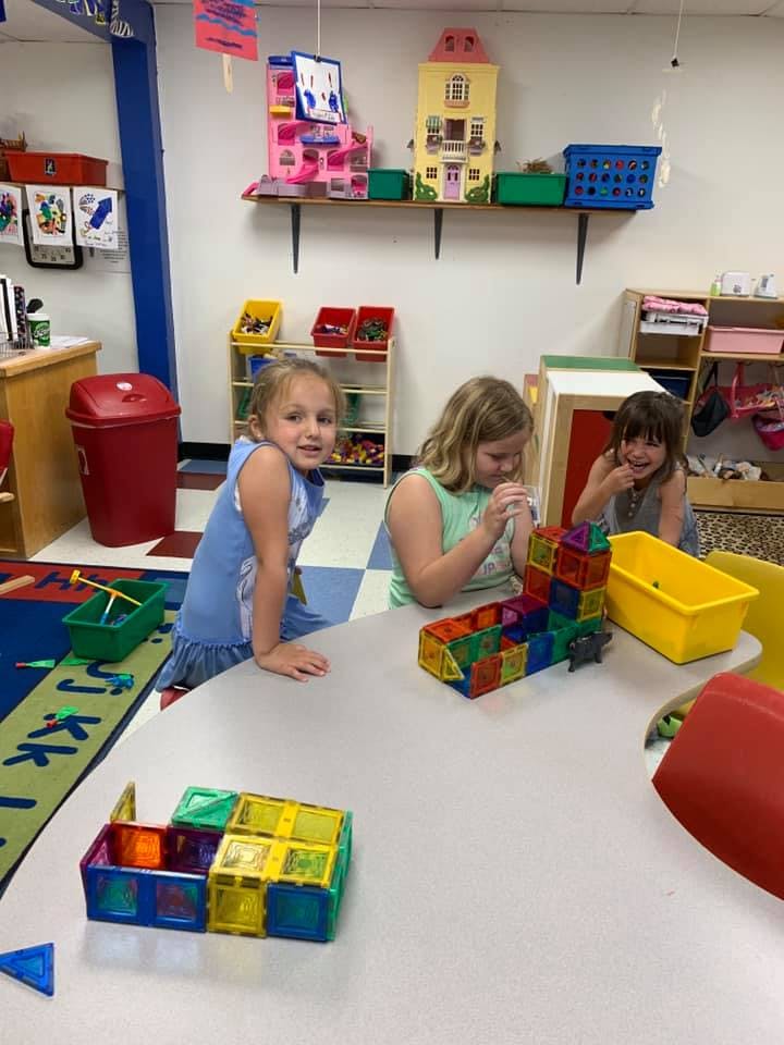Three children playing with magnetic blocks at a table in a classroom