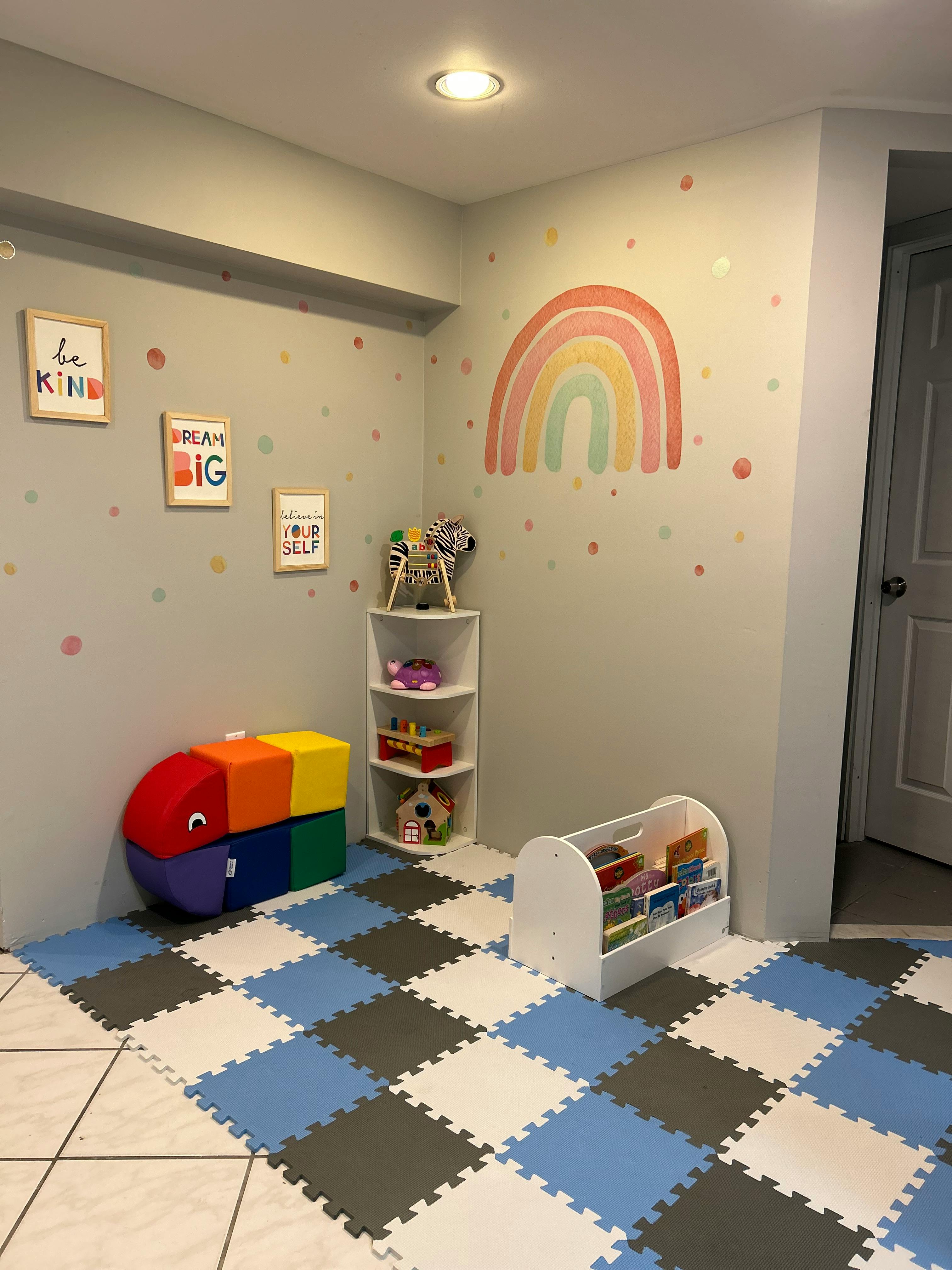 Playroom with rainbow wall decal, colorful floor mats, and toy storage