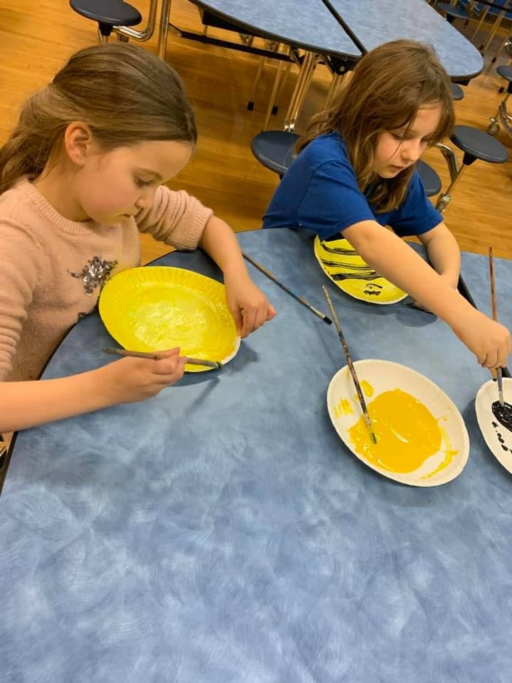 Two children painting yellow plates at a table