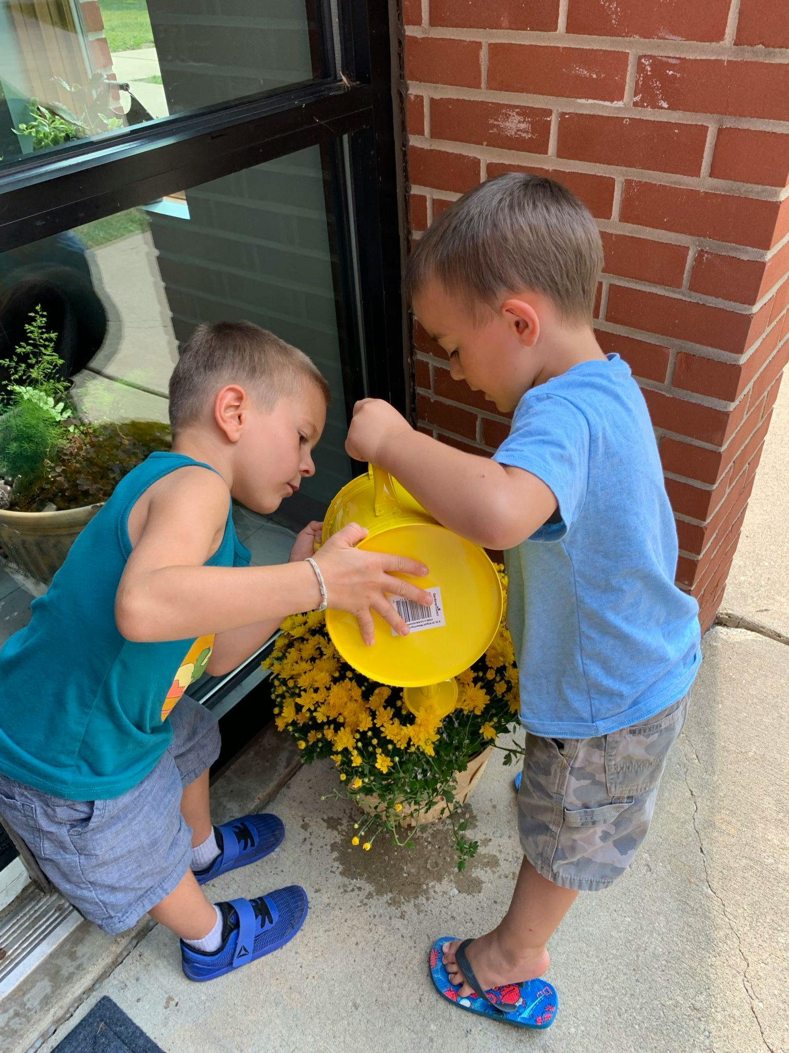 Two children watering a plant with a yellow bucket
