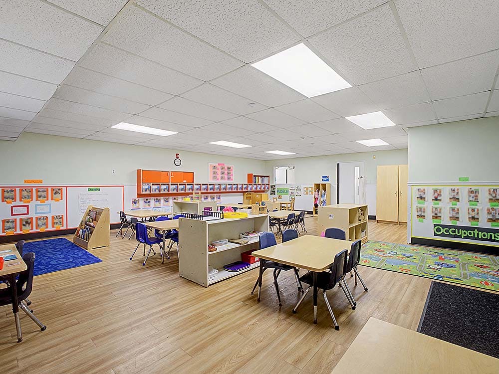 empty preschool classroom with tables and chairs, educational posters on walls