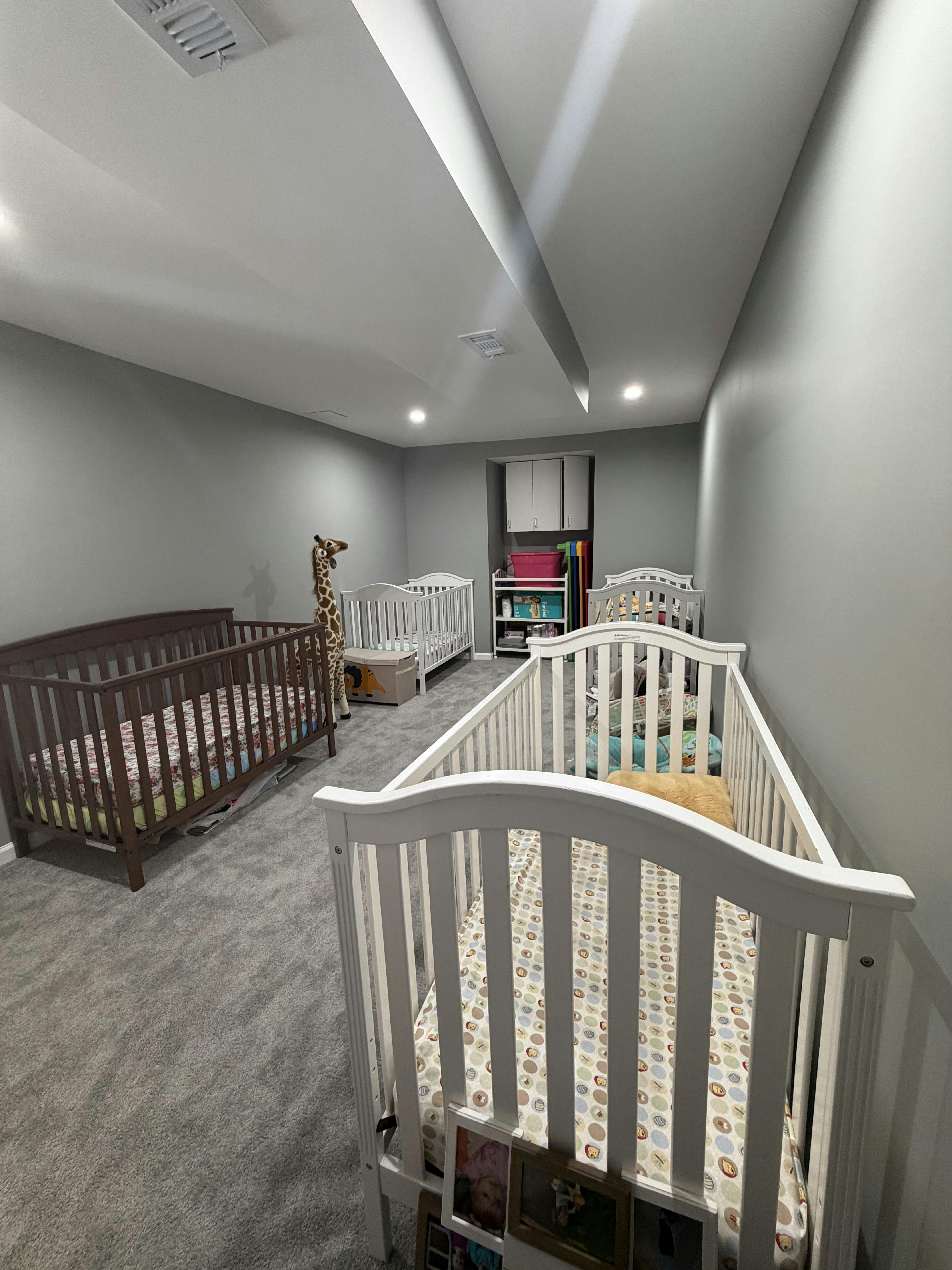 Room with four cribs and a tall giraffe stuffed animal