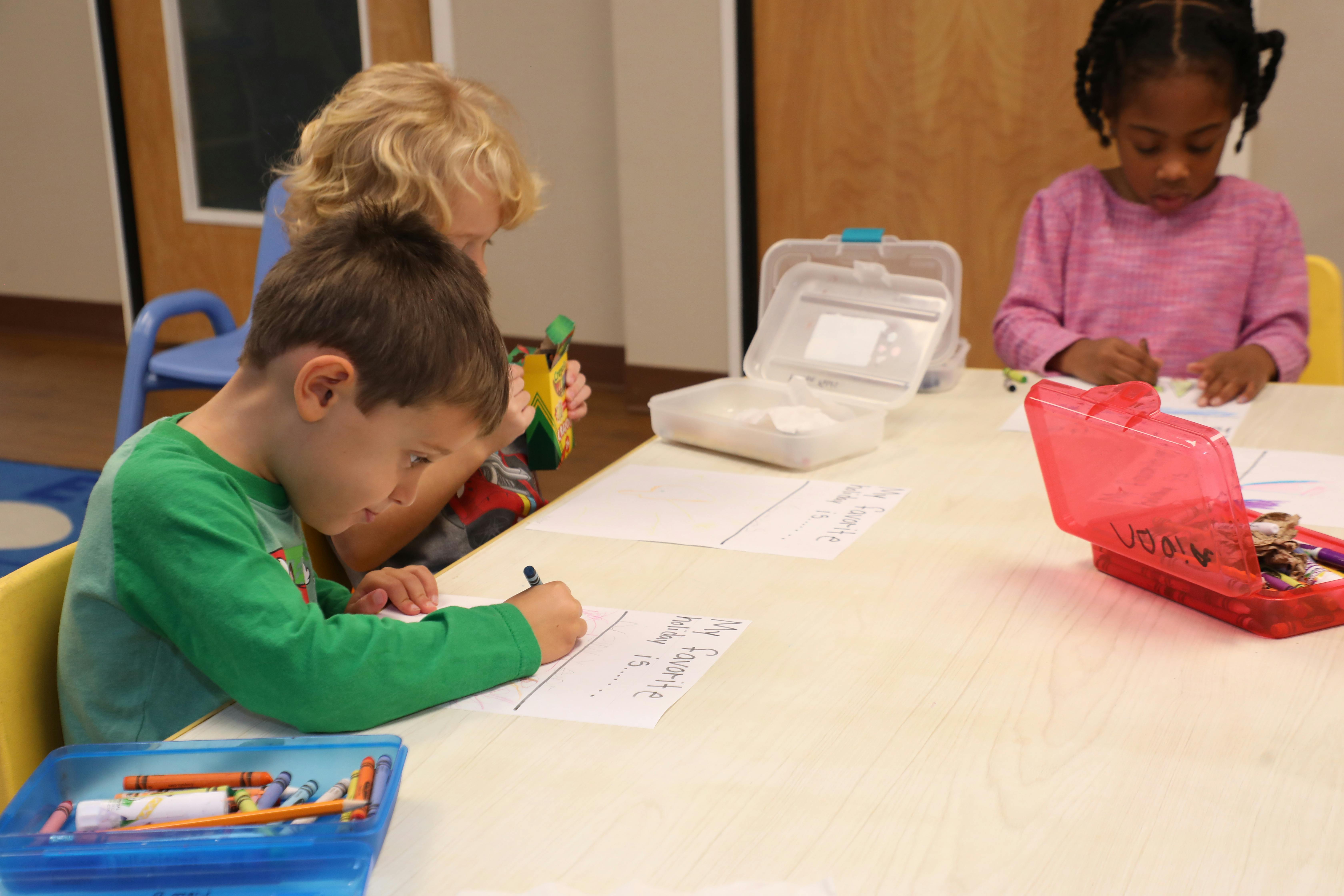 Three children drawing at a table in a classroom