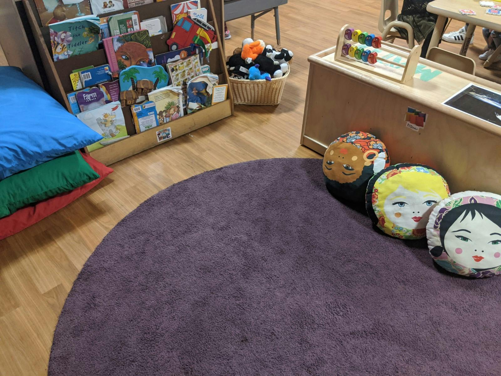 Classroom with a purple rug, colorful pillows, and a bookshelf