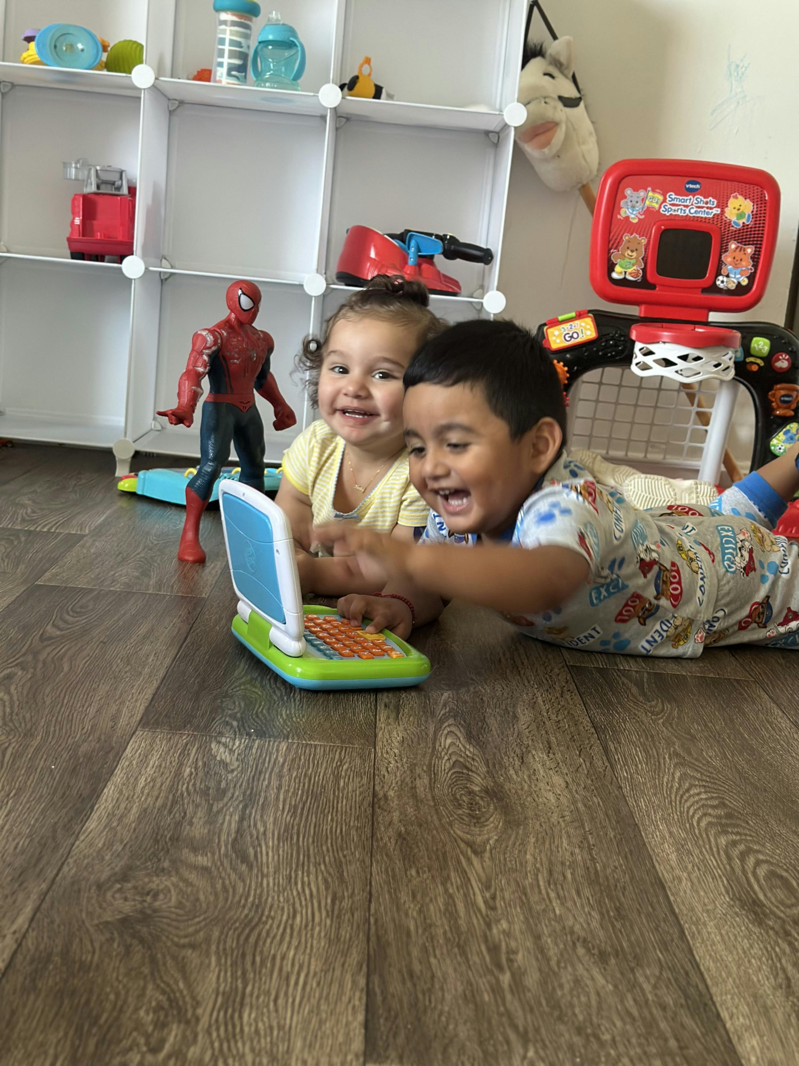 Two children lying on the floor playing with a toy laptop