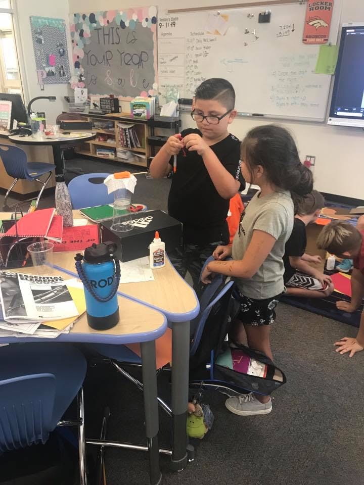 Two children standing in a classroom, one holding an object