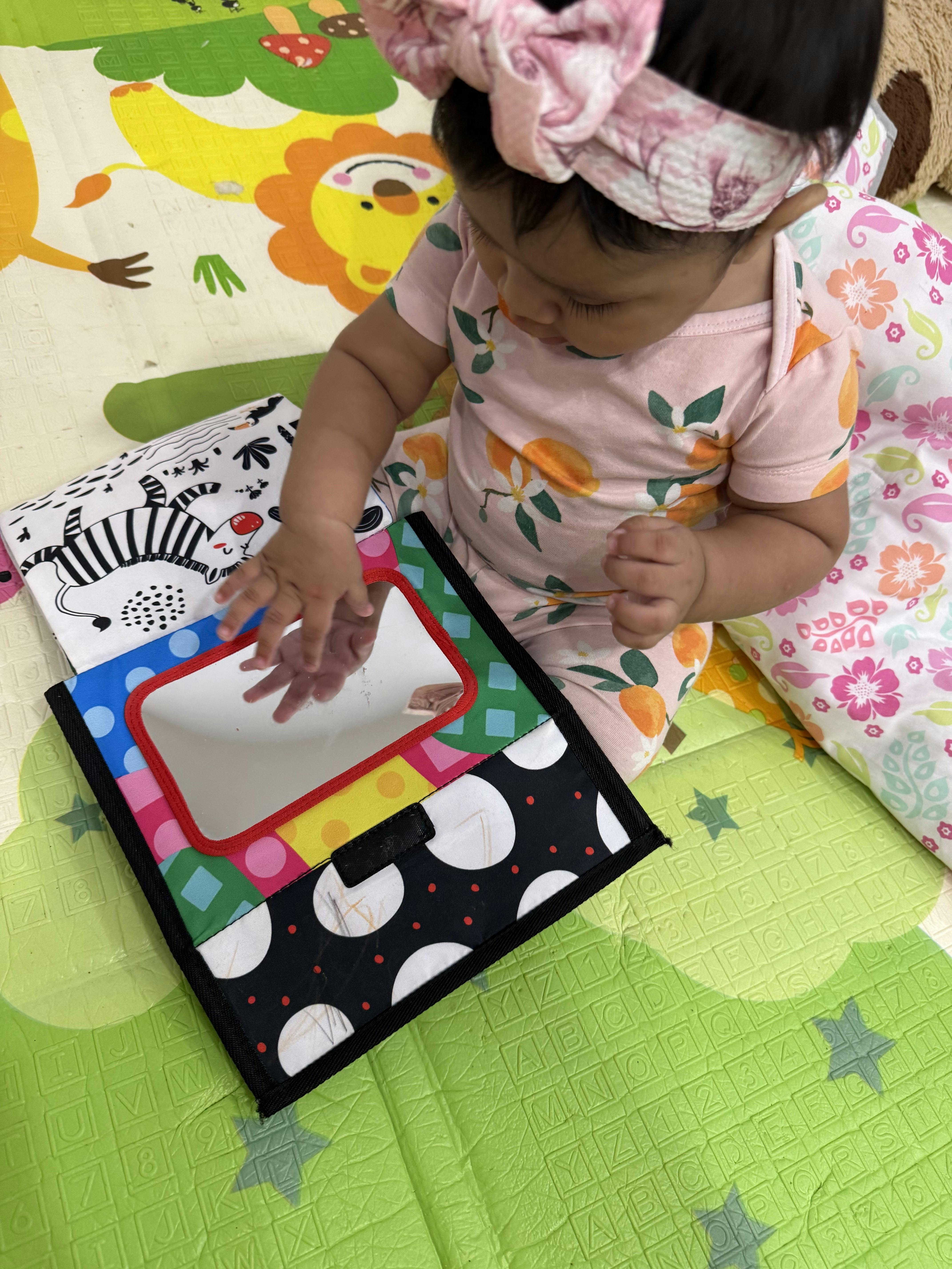 Child sitting on a play mat touching a toy mirror