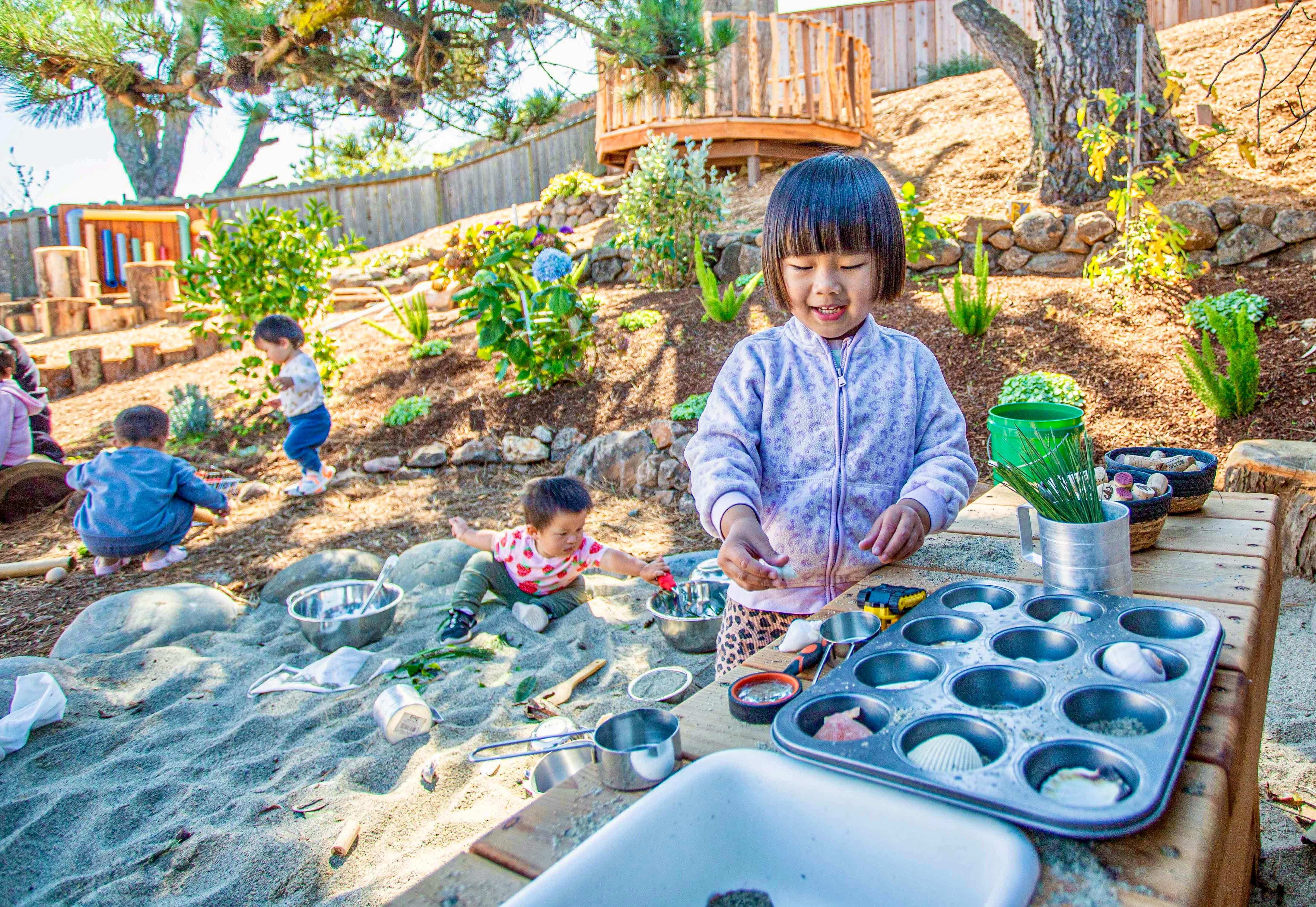 Child playing with sand and kitchen utensils in an outdoor play area