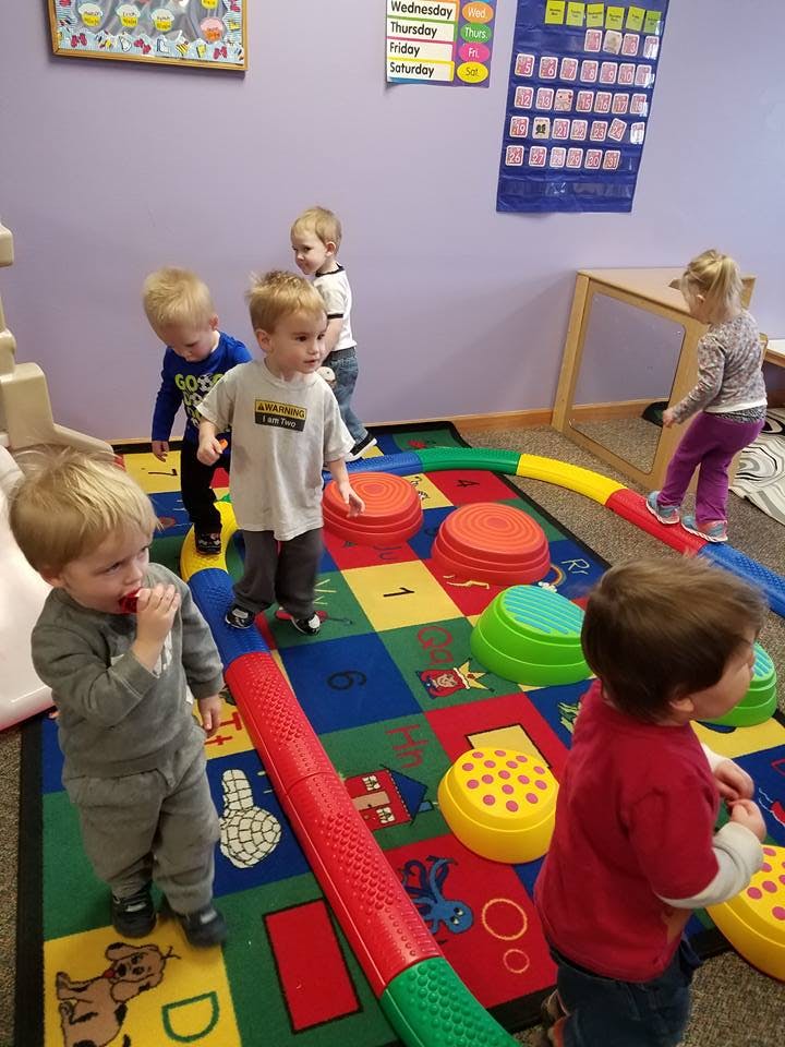 Children playing on a colorful rug with stepping stones and balance beam