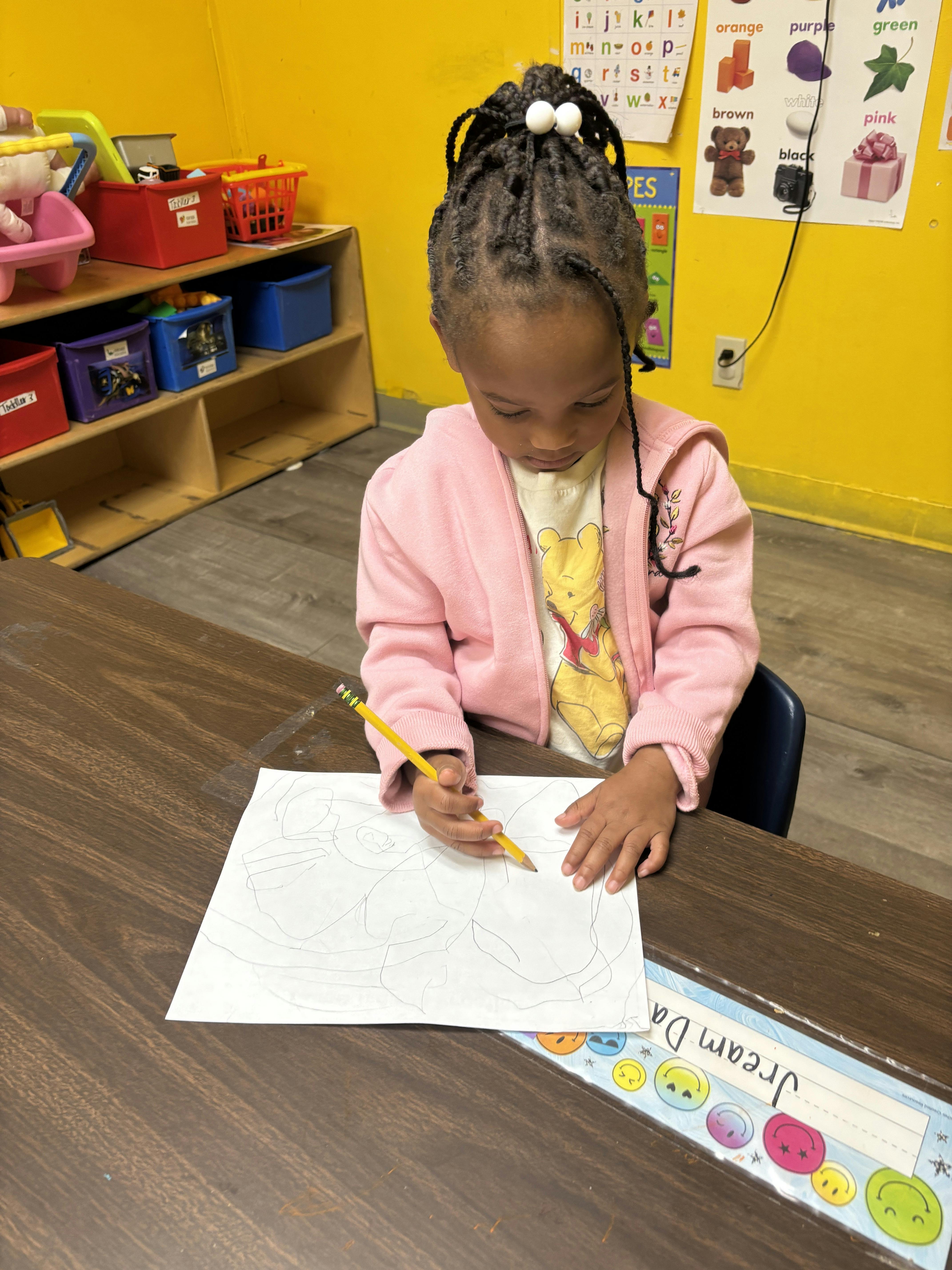 Child drawing on paper with a pencil at a table in a classroom