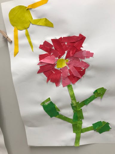 Paper collage of a red flower with a green stem and a yellow sun