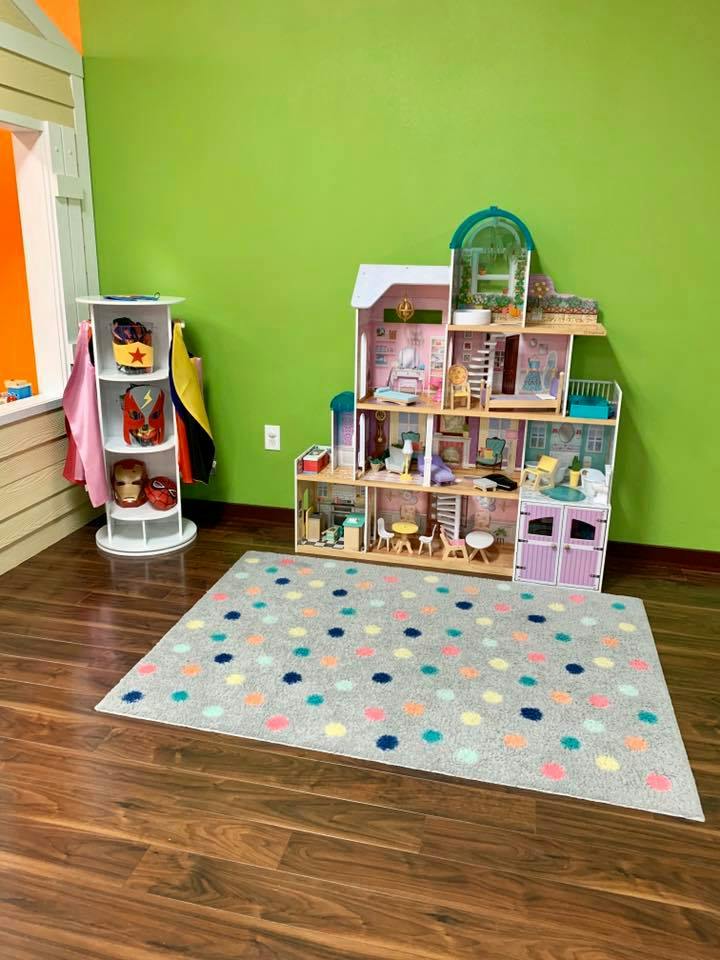 Dollhouse and toy shelf with a polka dot rug on a wooden floor