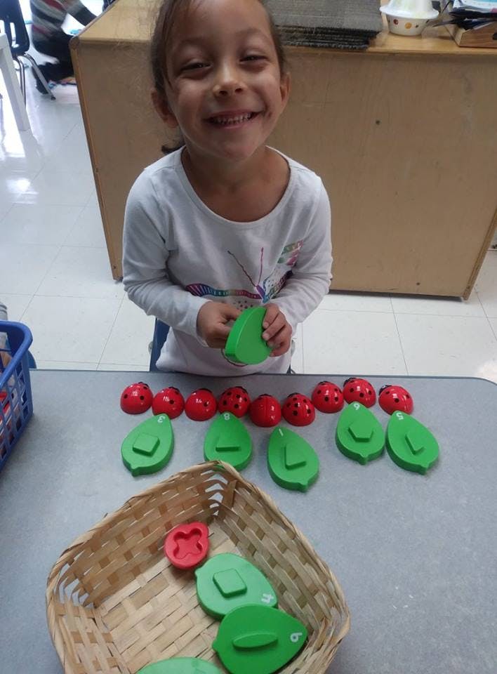 Child holding a green leaf shape, with red ladybug shapes and green leaf shapes on a table