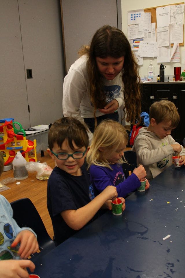 Person observing children at a table with small cups