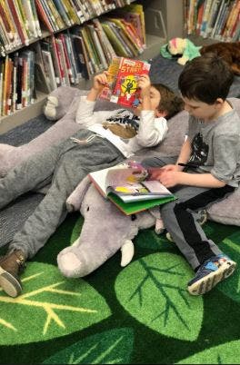 Two children reading books on the floor in a library