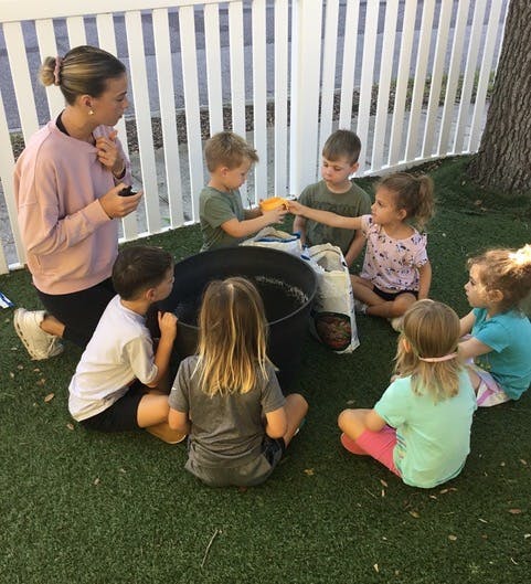 Adult and children gathered around a large pot outdoors