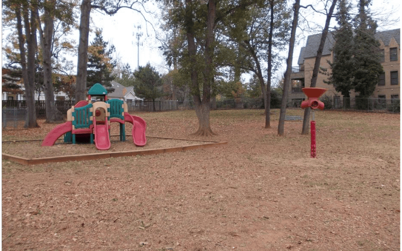 Playground set with slides on woodchips next to a red pole with a spinning toy