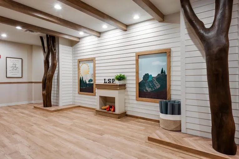 Room with wood floors, white walls, exposed beams, and tree-like pillars
