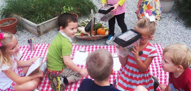 Children sitting on a red and white checkered blanket looking at items