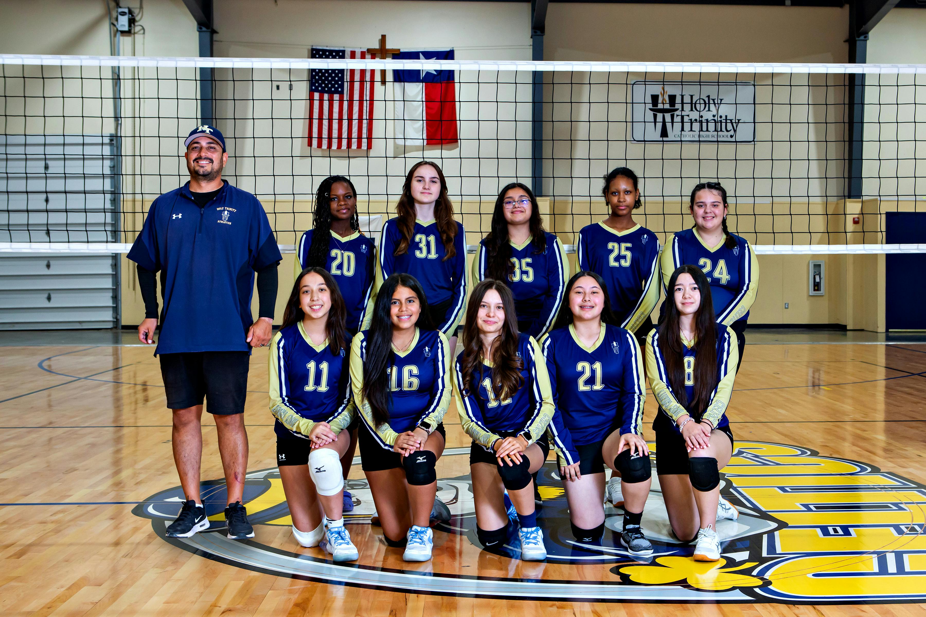 A coach and a team of teens in volleyball uniforms posing for a group photo