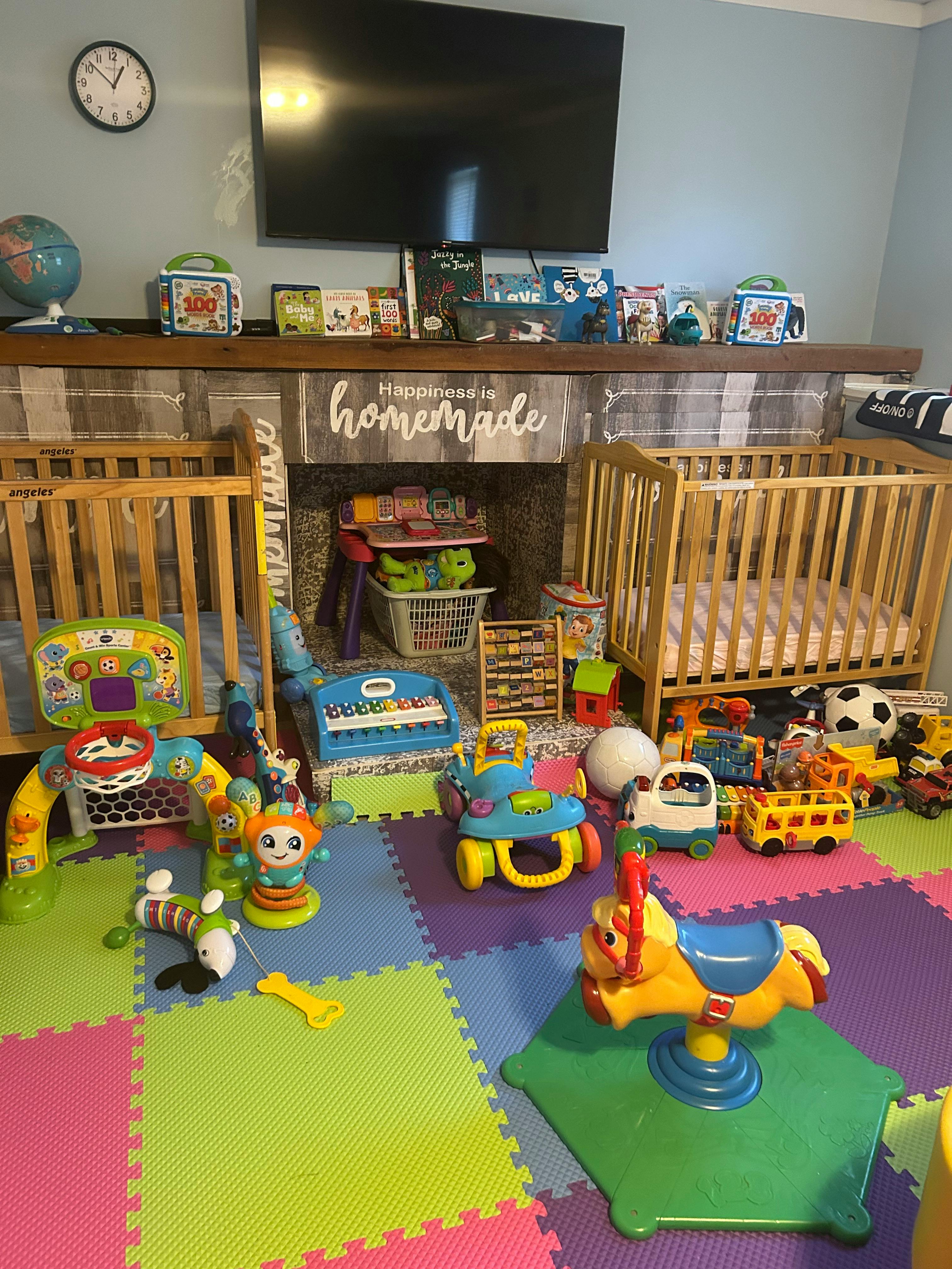 Two cribs in a room filled with children's toys and playmats