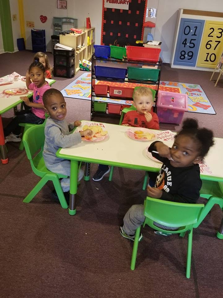 Four children sitting at tables in a classroom