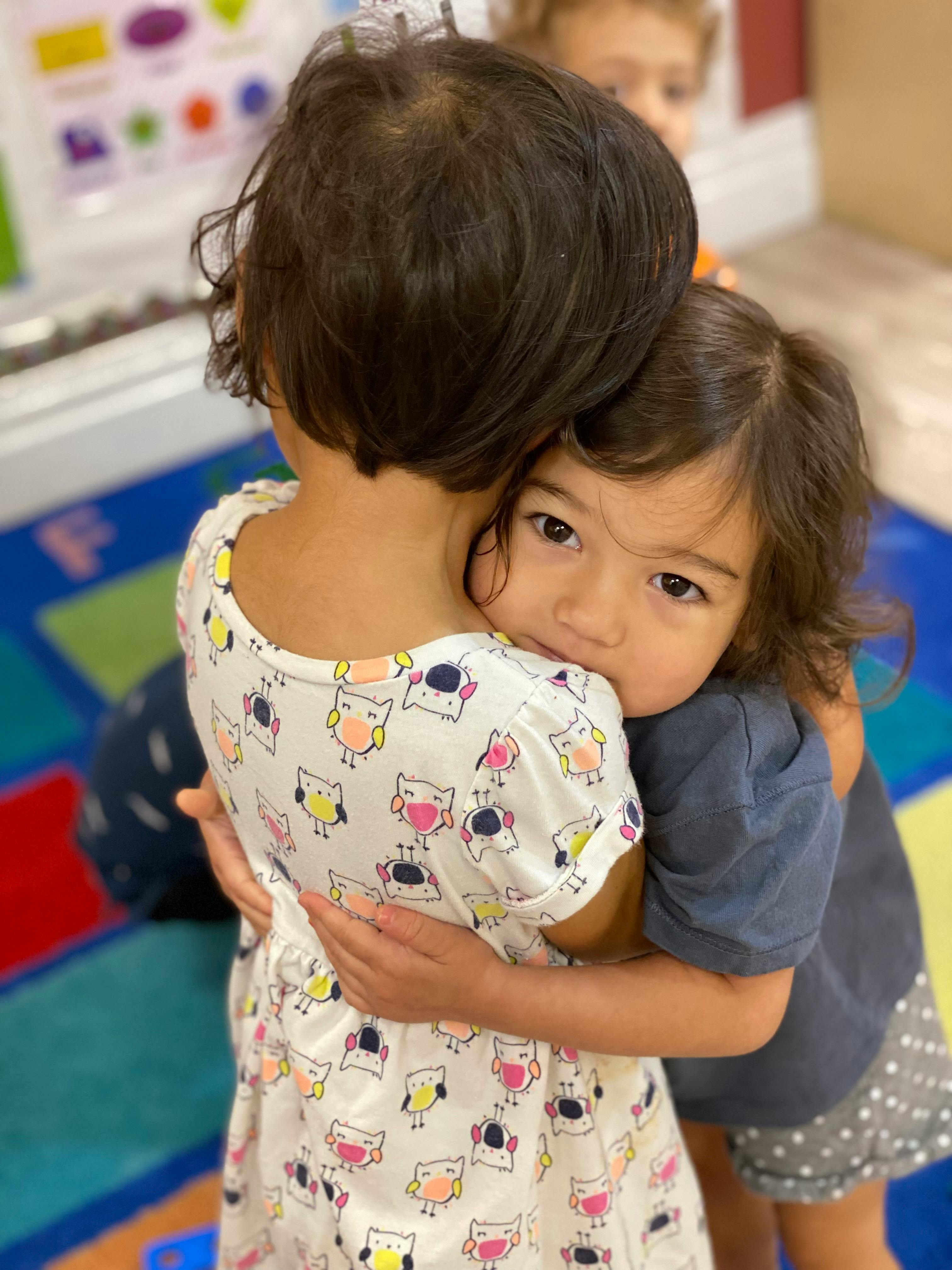 Two children hugging, one looking over the other's shoulder