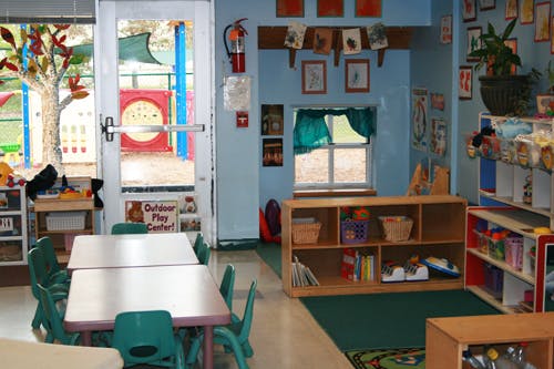 Classroom with small tables and chairs, shelves, and a door to an outdoor play area