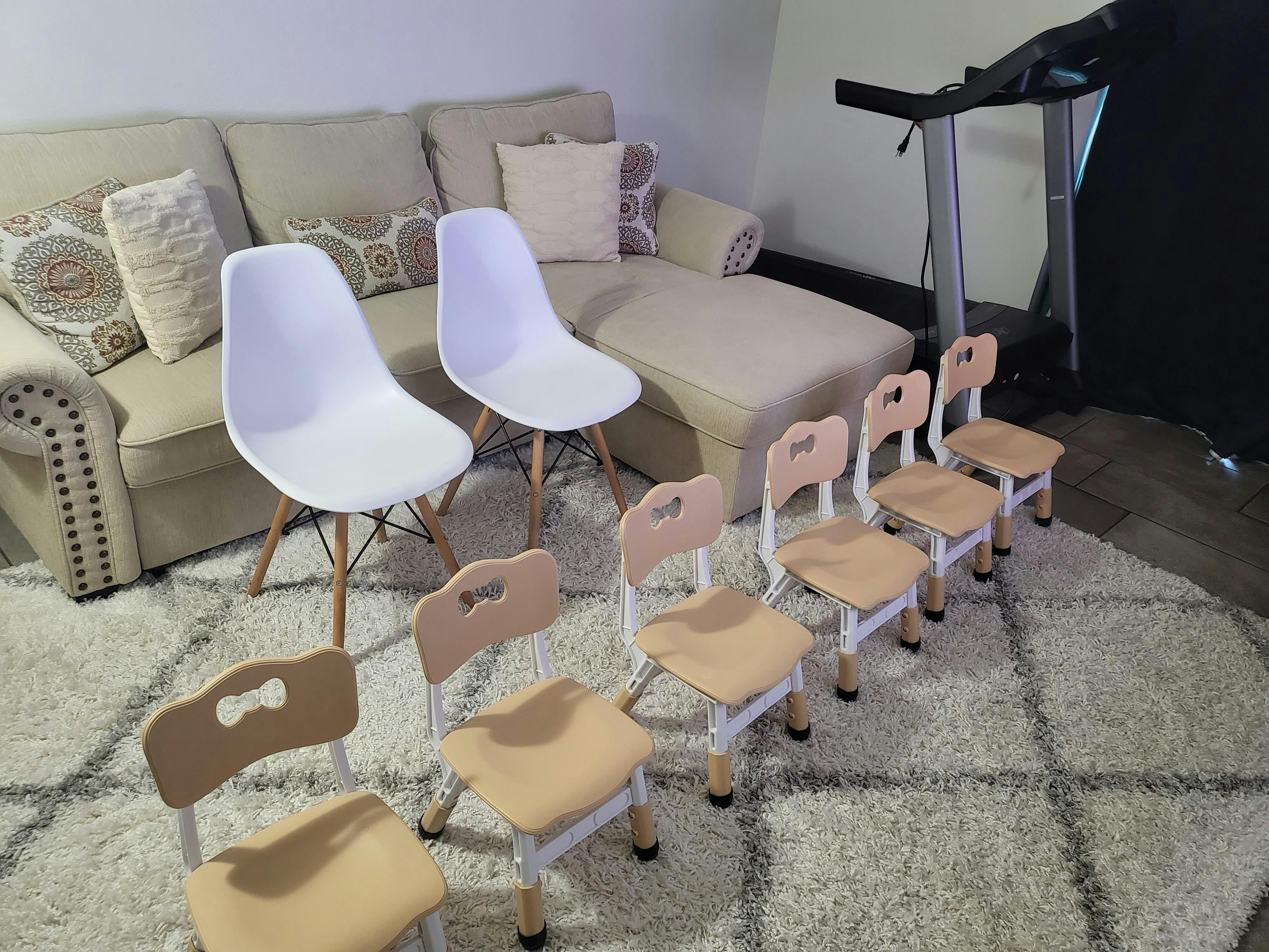 Two white chairs and five small wooden chairs in front of a sofa