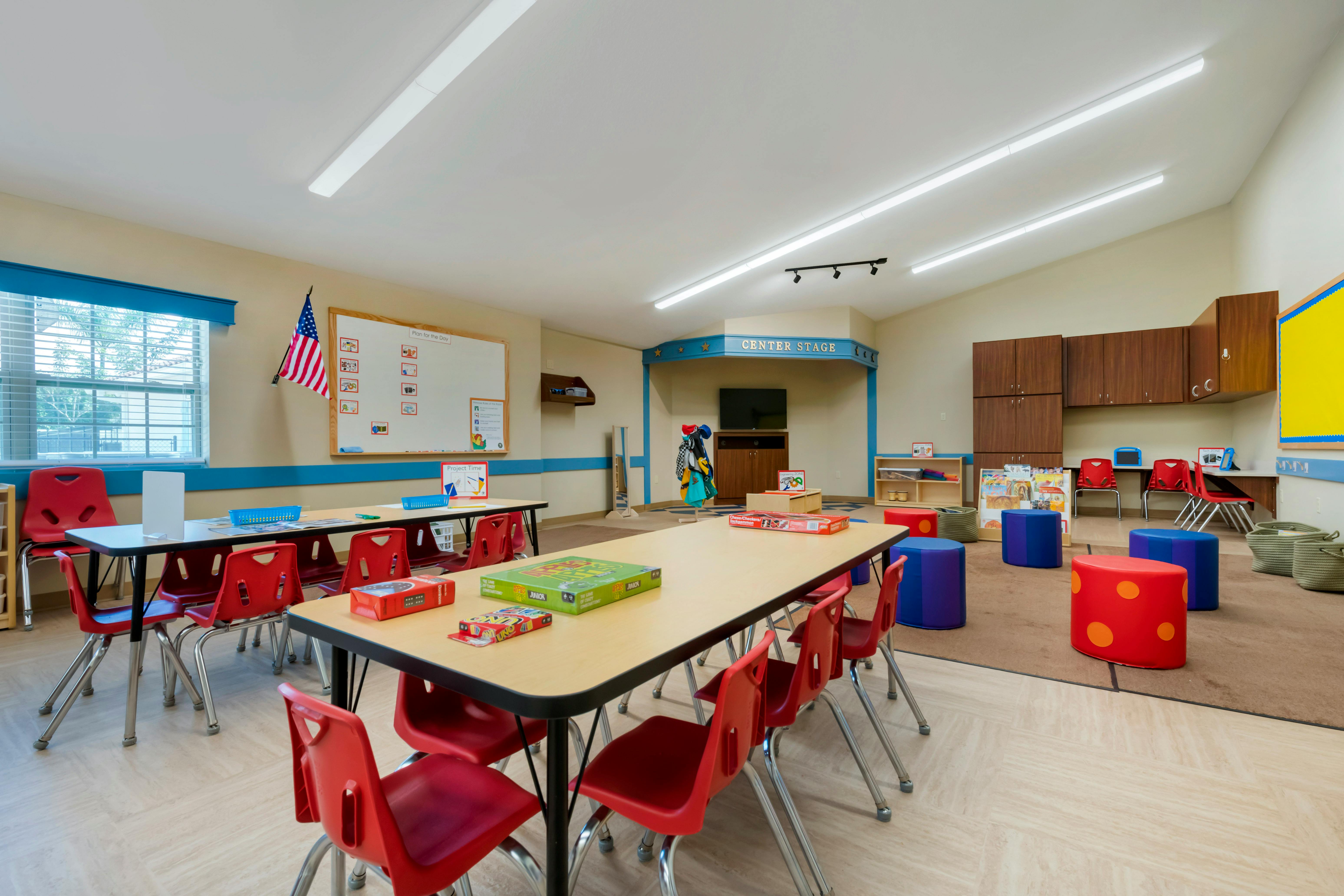 Classroom with child-sized tables and chairs, a whiteboard, and a play area labeled "CENTER STAGE"