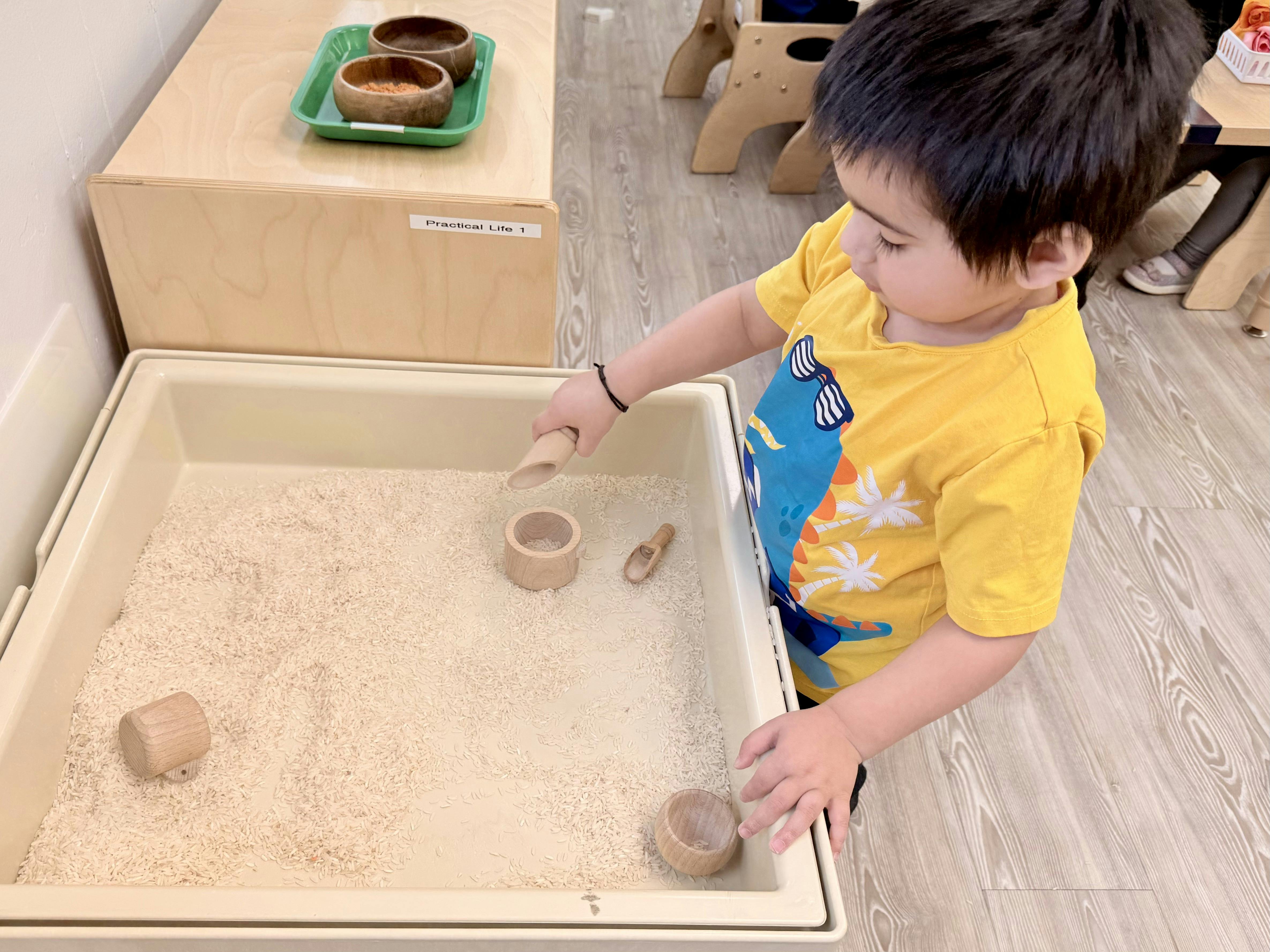 Child playing with rice in a bin with a scoop and wooden cups