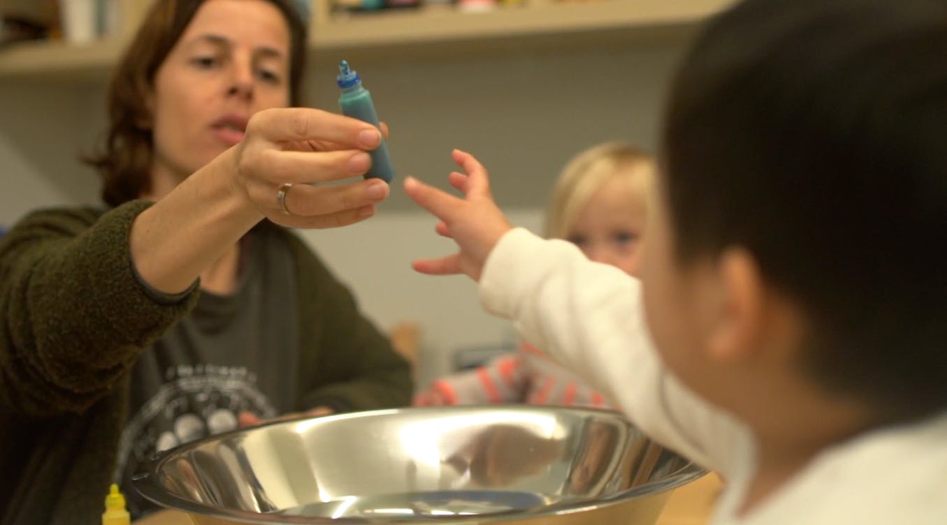 Person holding up a small object to a child reaching out
