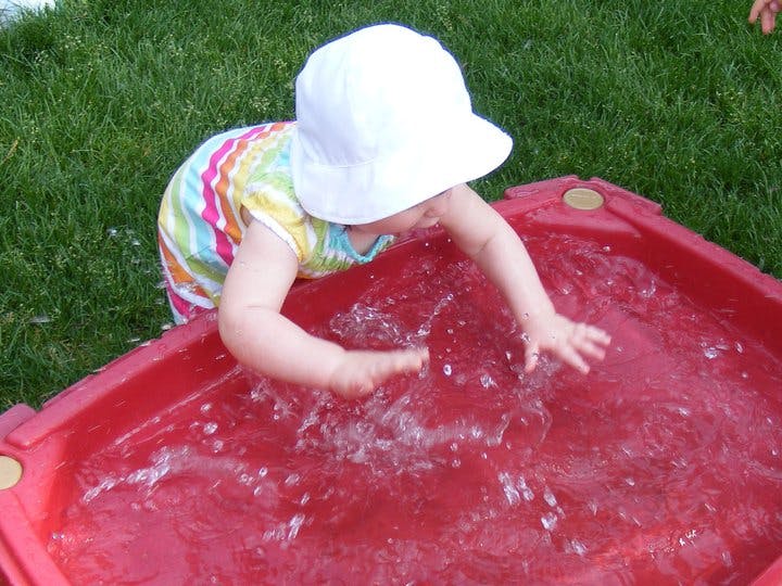 Child in a white hat playing in a red water table
