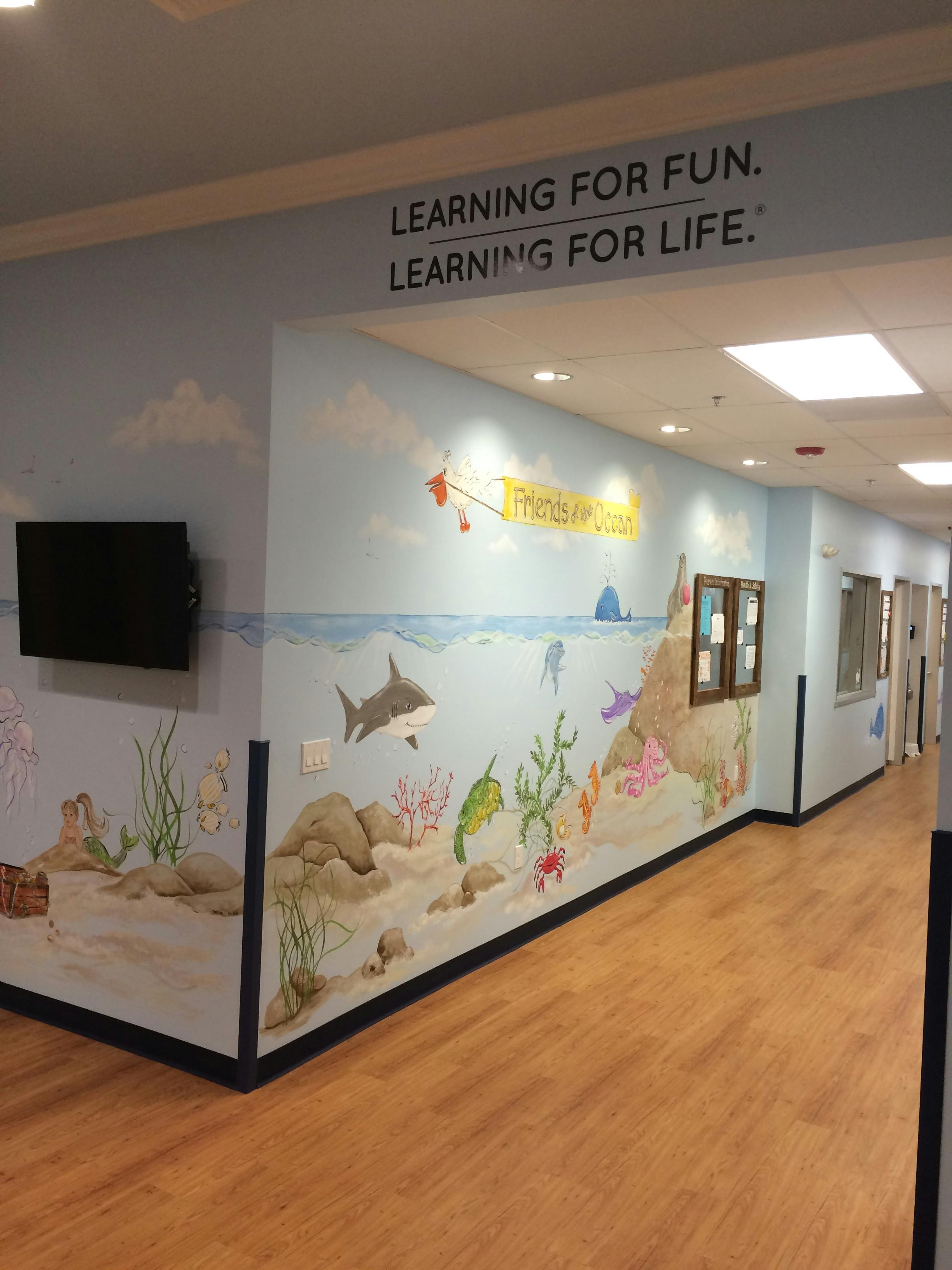 Hallway with ocean-themed mural and text "LEARNING FOR FUN. LEARNING FOR LIFE."