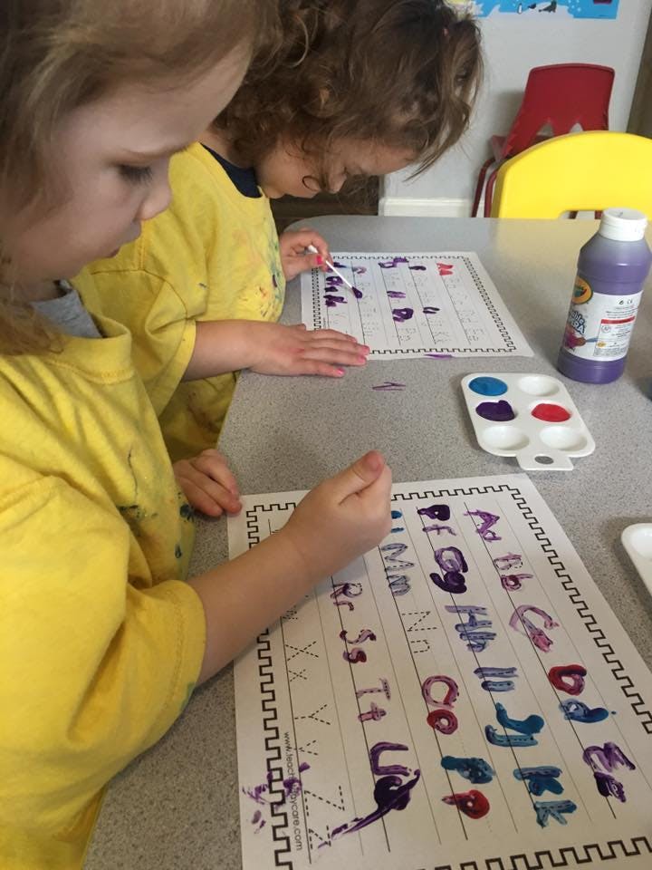 Two children painting letters on paper