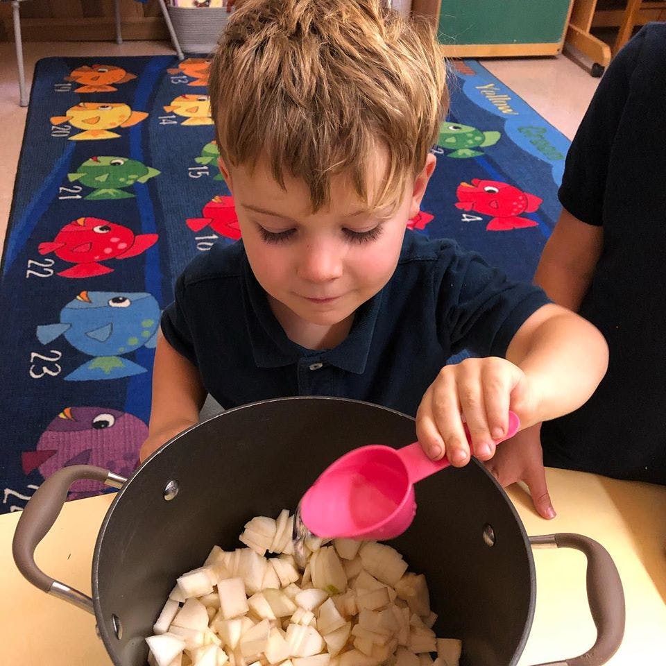 Child scooping diced food from a pot with a pink spoon